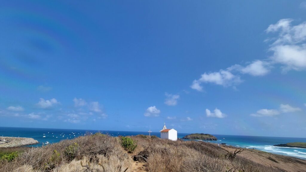 a small white church looking over a blue sea with a blue sky